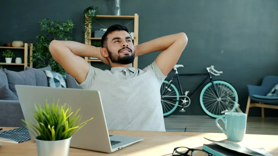 Man relaxing at desk with laptop and bicycle.