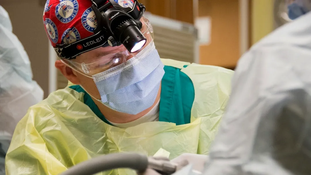 Surgeon wearing surgical cap and mask performing procedure.