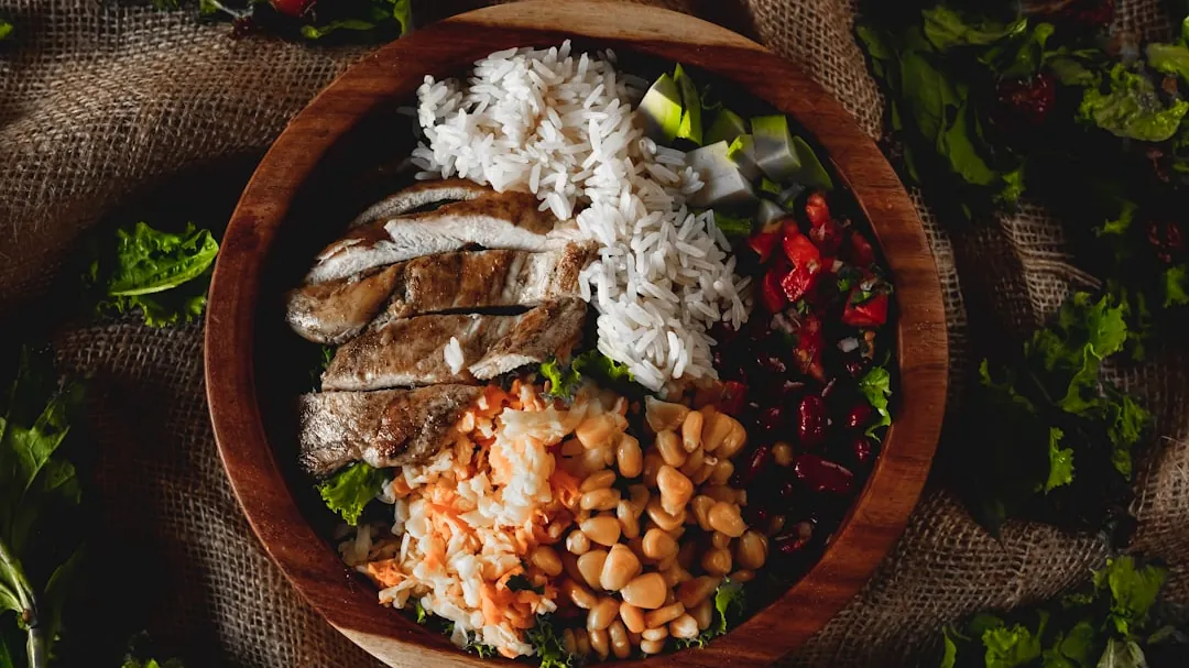A wooden bowl filled with chicken, rice, and beans.