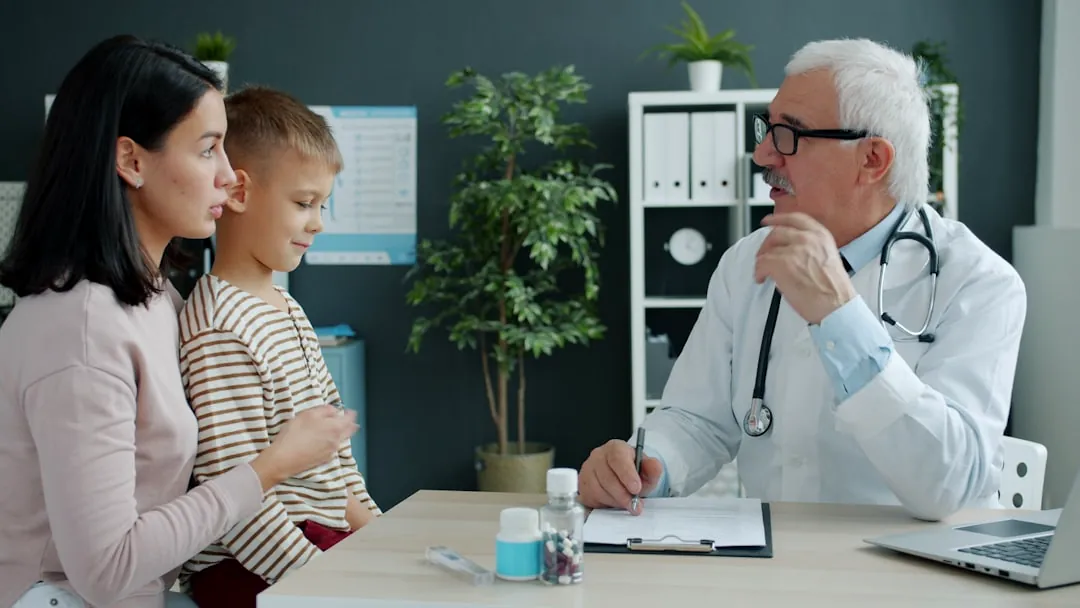 Doctor talking to mother and child at desk.