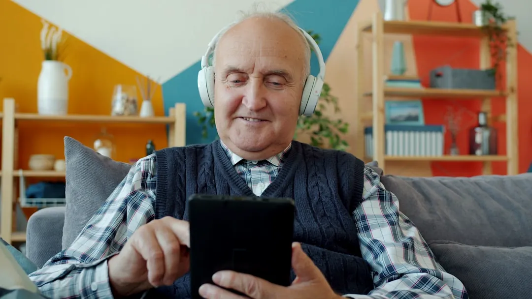 Elderly man with headphones uses a tablet.