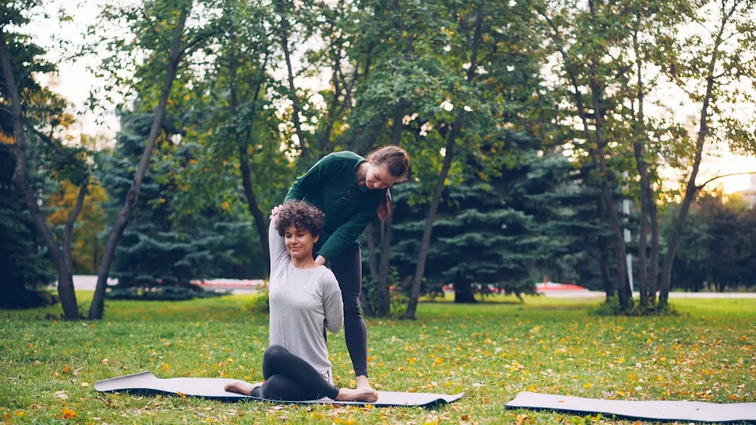 Instructor assisting woman with yoga pose in park
