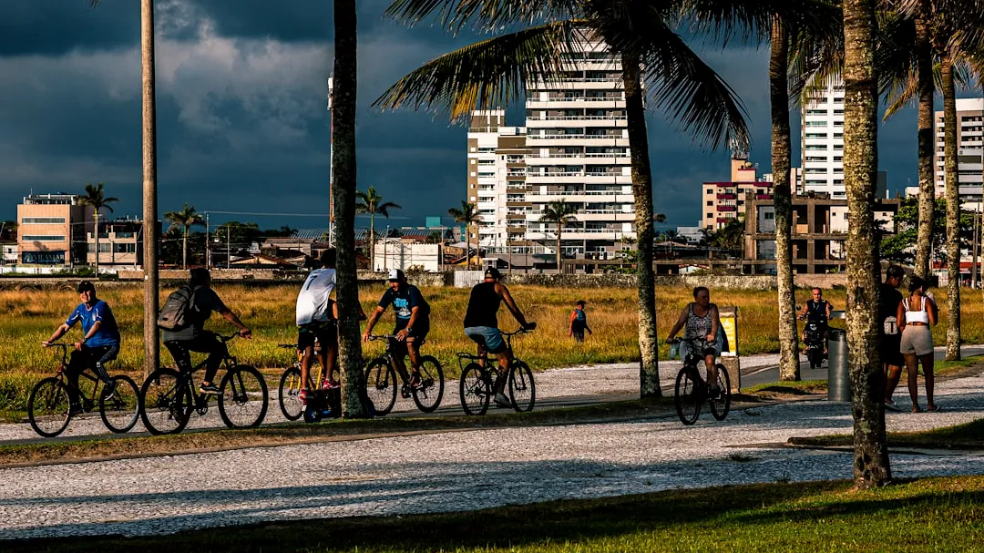 People cycling on a path with palm trees and buildings.