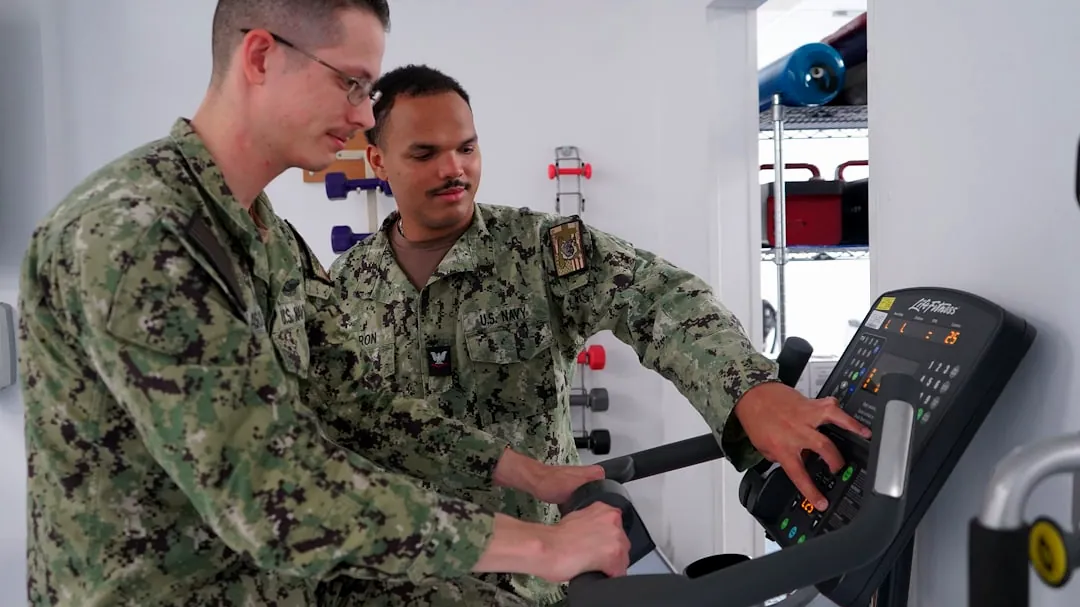 Two men in military uniforms on exercise bike.