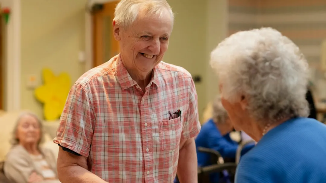 Two smiling seniors talking in a common room.