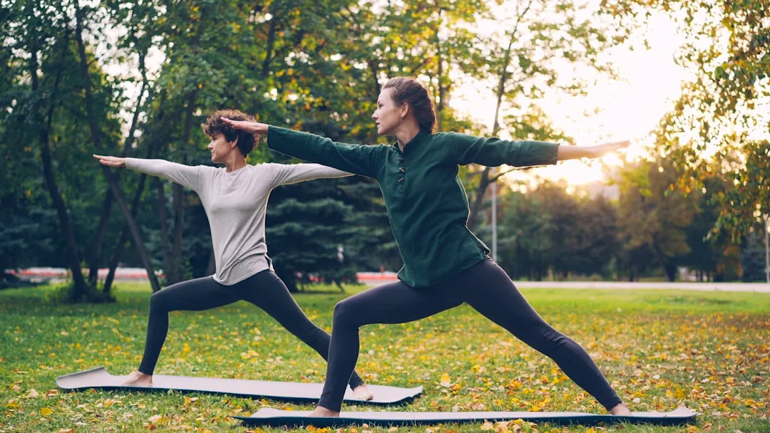Two women practicing yoga warrior pose outdoors.