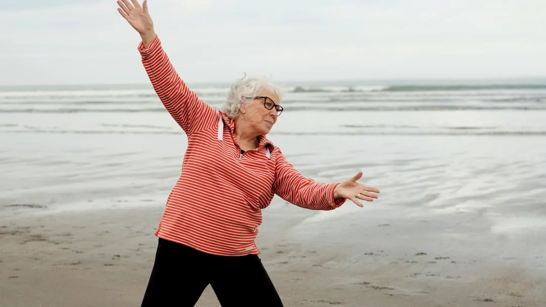 Woman exercises at the beach with outstretched arms.