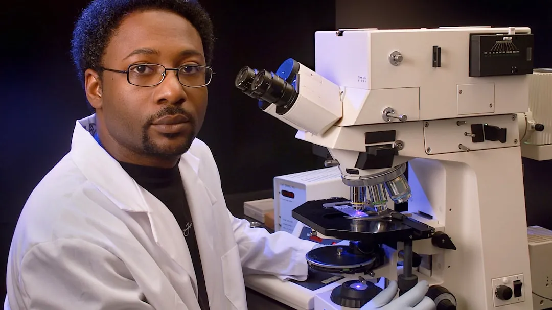 a man in a lab coat is looking into a microscope