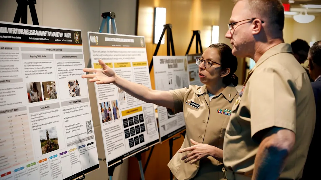 Two people in uniform discuss a presentation board of posters